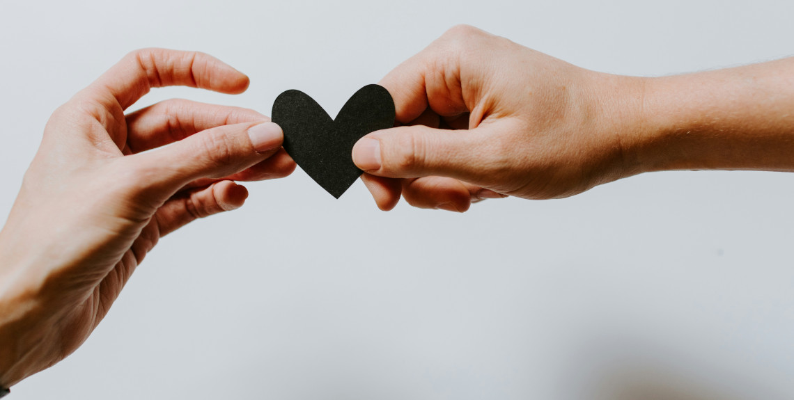 Zwei Hände halten ein schwarzes Herz aus Papier Zwei Hände halten ein schwarzes Herz aus Papier